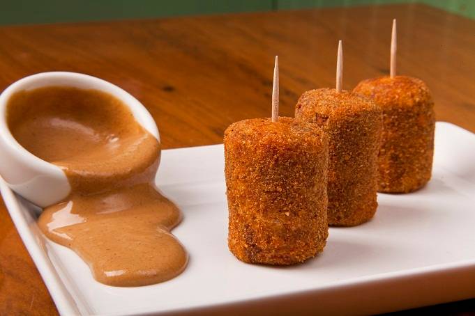 Mini croquetes de carne recheados com queijo e servidos com molho de mostarda s&atilde;o boa op&ccedil;&atilde;o de entrada dispon&iacute;vel no menu promocional<br>