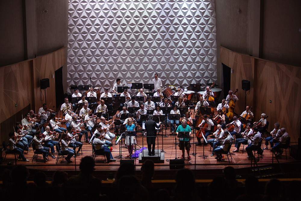 Músicos da OSB se apresentando sobre o tablado de madeira da sala, tendo ao fundo a parede com texturas do espaço