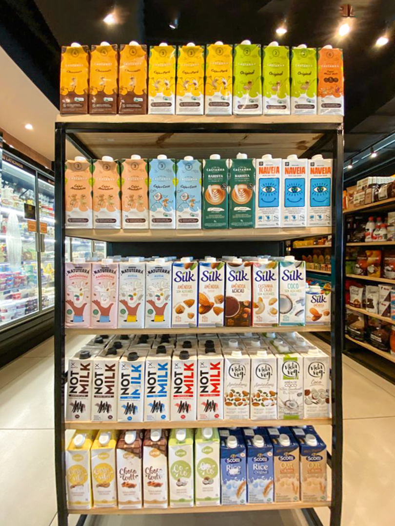 La Fruttaria.jpeg A imagem mostra uma seção de leites vegetais de um mercado com várias marcas disponíveis nas prateleiras