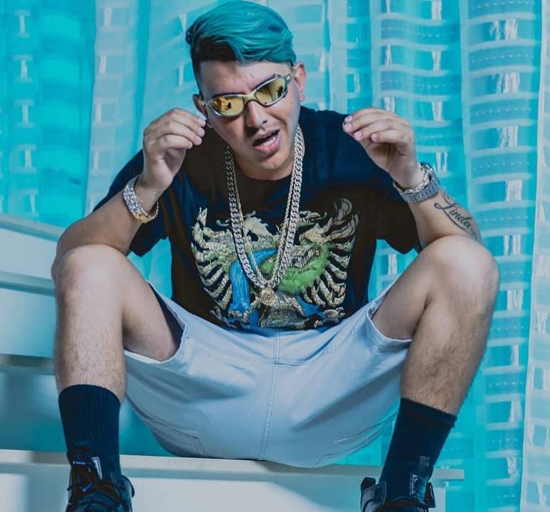 MC Fioti sentado, com as pernas abertas e as mãos perto do rosto