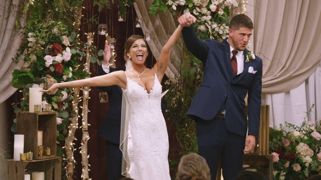 Casal de noivos no altar, com as mãos dadas e os braços para cima