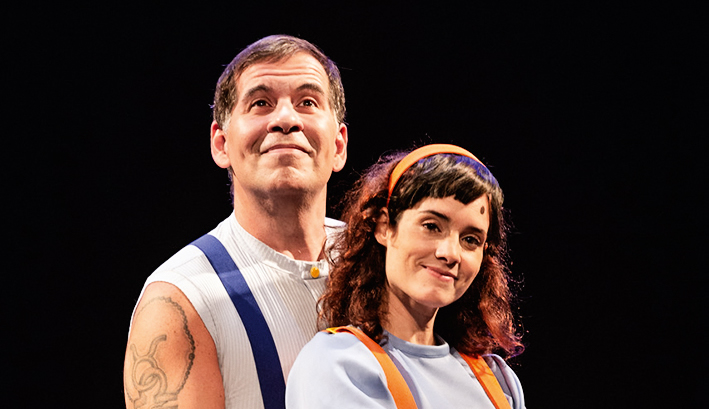 Leandro Hassum e Elisa Pinheiro abraçados no palco, com figurinho colorido