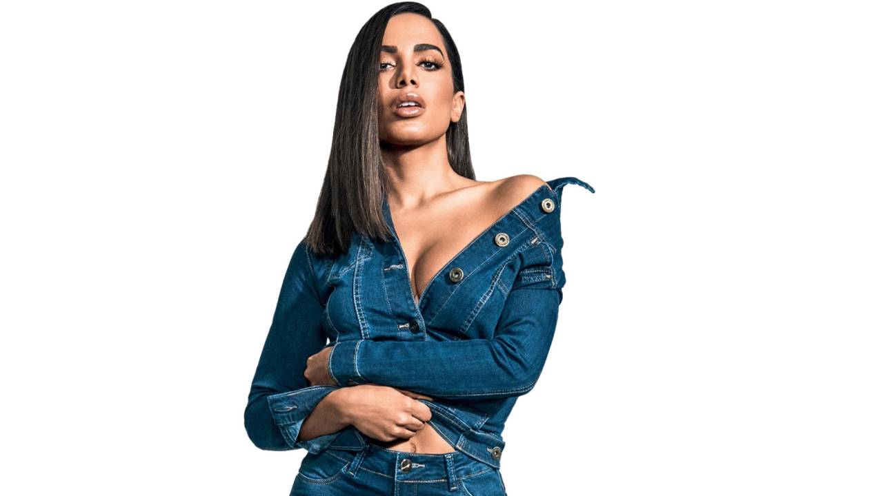 Cantora Anitta com uma blusa jeans bastante decotada e cabelo liso cruza os braços na cintura