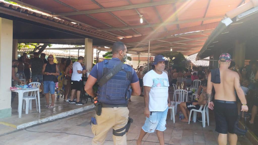 A imagem mostra agentes da Guarda Municipal em meio a algumas pessoas, num jardim