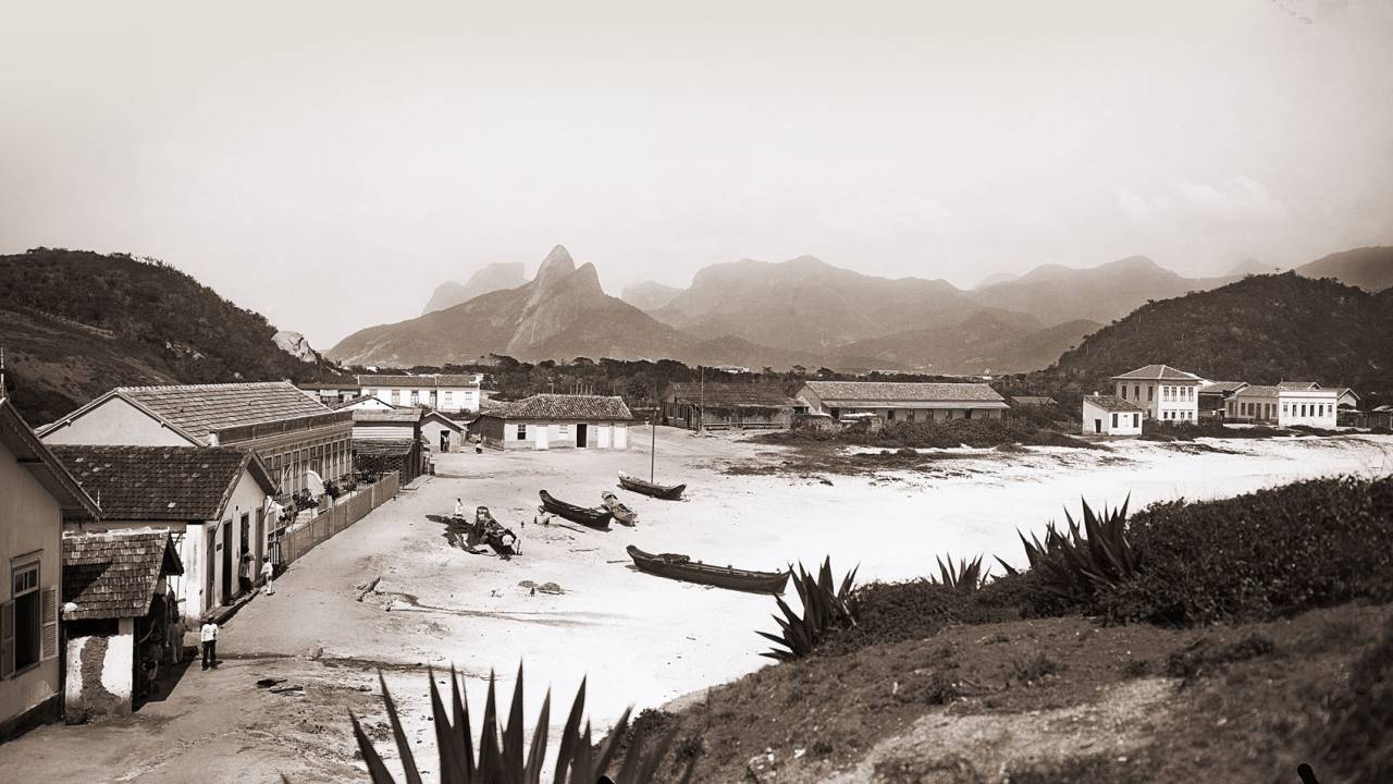 Imagem de 1895 mostra local onde hoje é o posto 6, em Copacabana. Há construções bem simples junto à areia e o Morro Dois Irmãos ao fundo