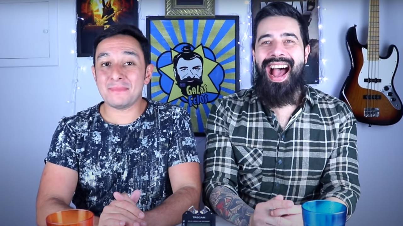 A imagem mostra Helder Maldonado e Marco Bezzi, sorrind para a câmera, tendo ao fundo a imagem símbolo do site de humor Galãs Feios