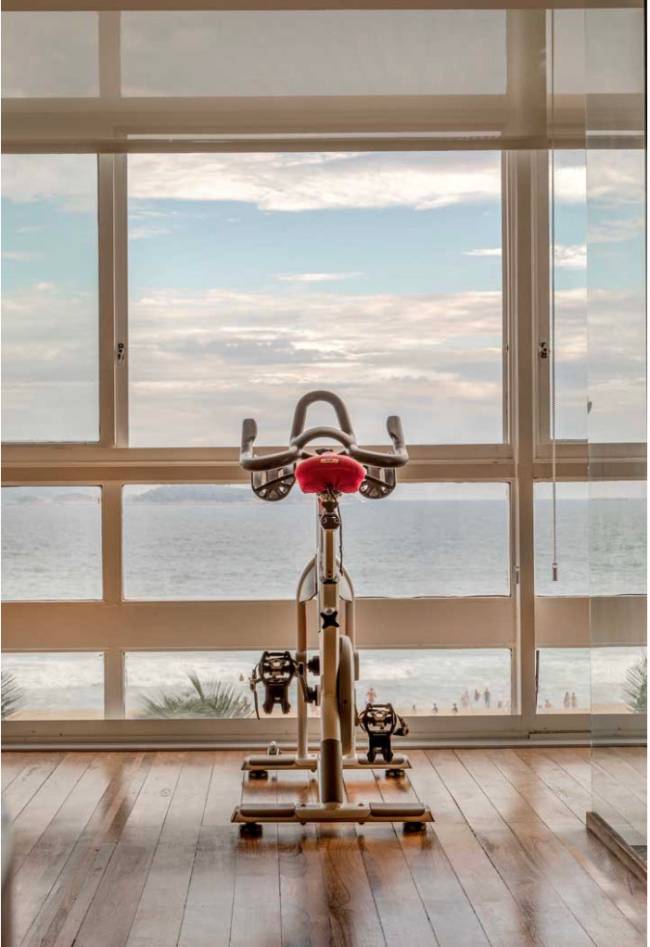 Pedalando com vista Imagem mostra a bicicleta na sala com vista para o mar.