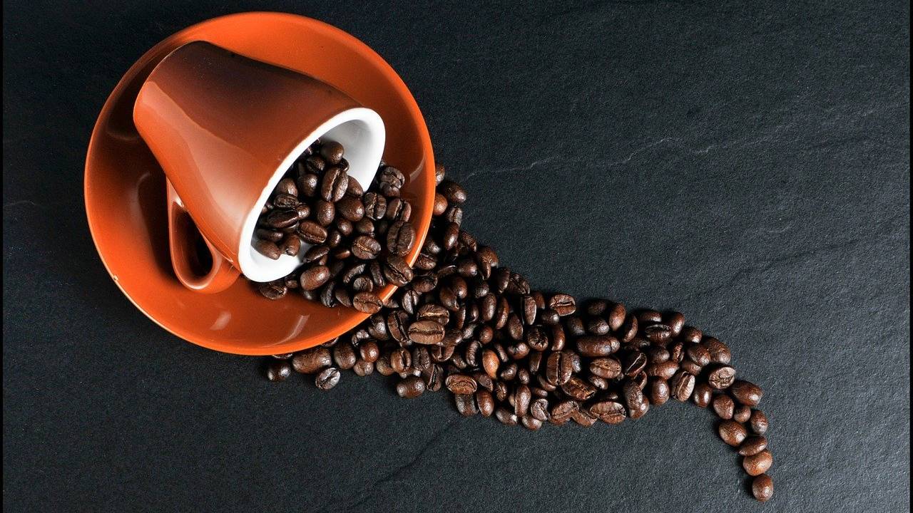 Xícara com grãos de café espalhados pela mesa