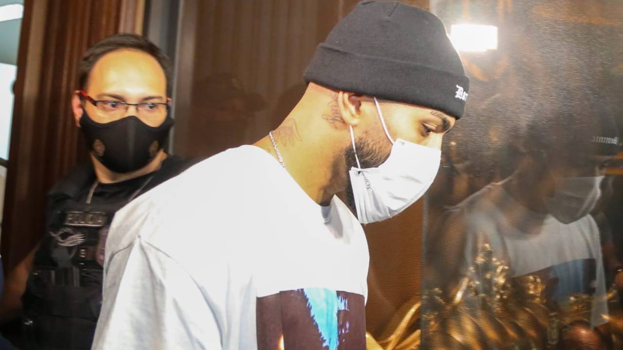 A imagem mostra o jogador Gabigol, cabisbaixo, de gorro preto e máscara, entrando numa sala