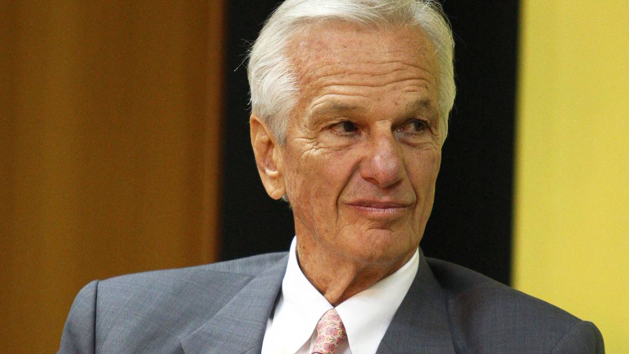 A imagem mostra o empresário Jorge Paulo Lemann, de terno e gravata, sorrindo