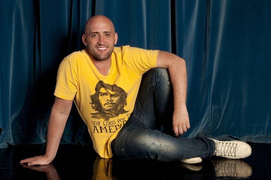A imagem mostra o ator Paulo Gustavo sentado no palco, vestindo uma camiseta amarela com o rosto de Che Guevara