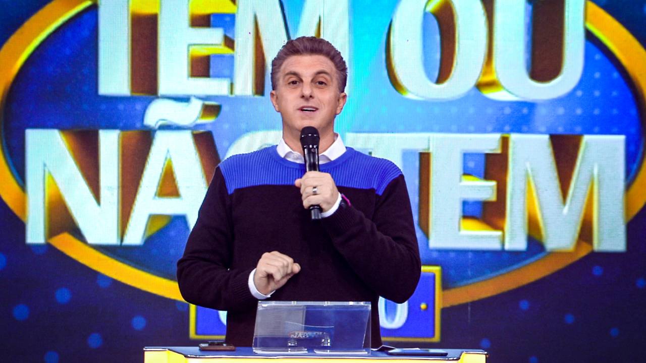 Luciano Huck no cenário de seu programa, segurando um microfone