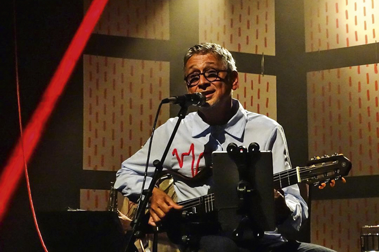 Zé Renato no palco, de óculos, tocando violão e cantando
