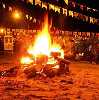 Uma grande fogueira de São João pegando fogo entre várias bandeirinhas de Festa Junina