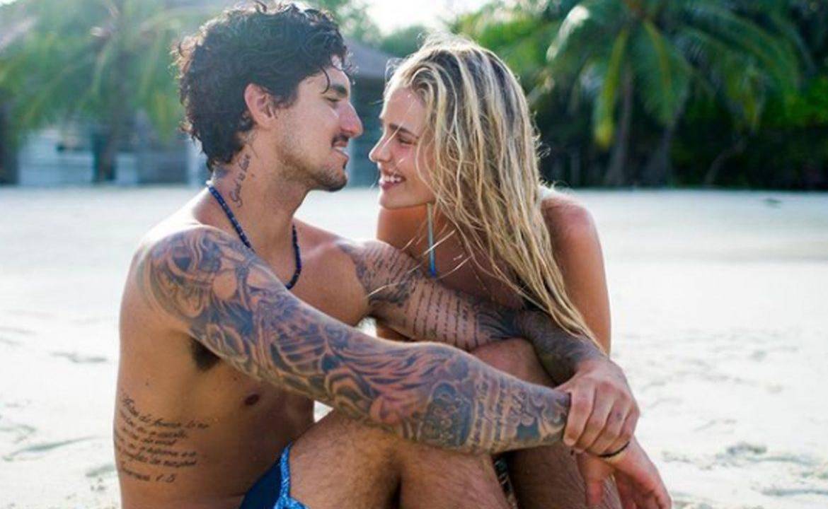 A imagem mostra Gabriel Medina e Yasmin Brunet na praia, sentados na areia