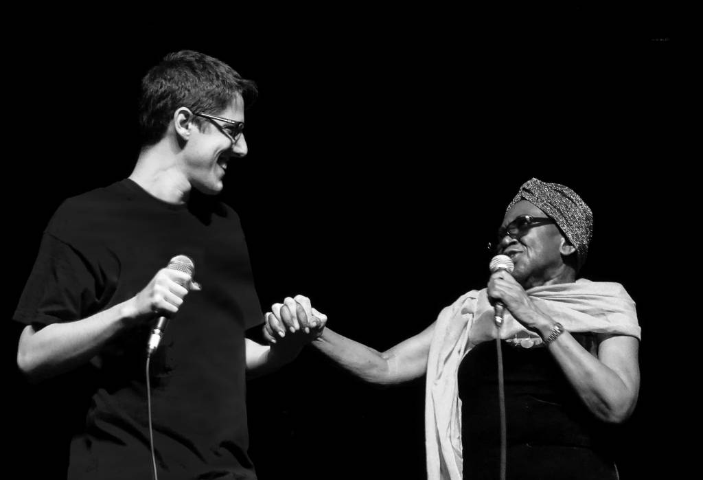 JOAO E AUREA CAPA DO ENCARTE Cantores João Senise e Áurea Martins no palco, segurando microfones e dando as mãos um para o outro