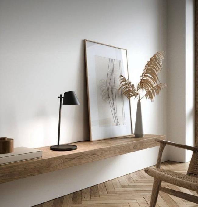 Estilo escandinavo A imagem mostra uma bancada com madeira clara, quadro apoiado e uma luminária de mesa