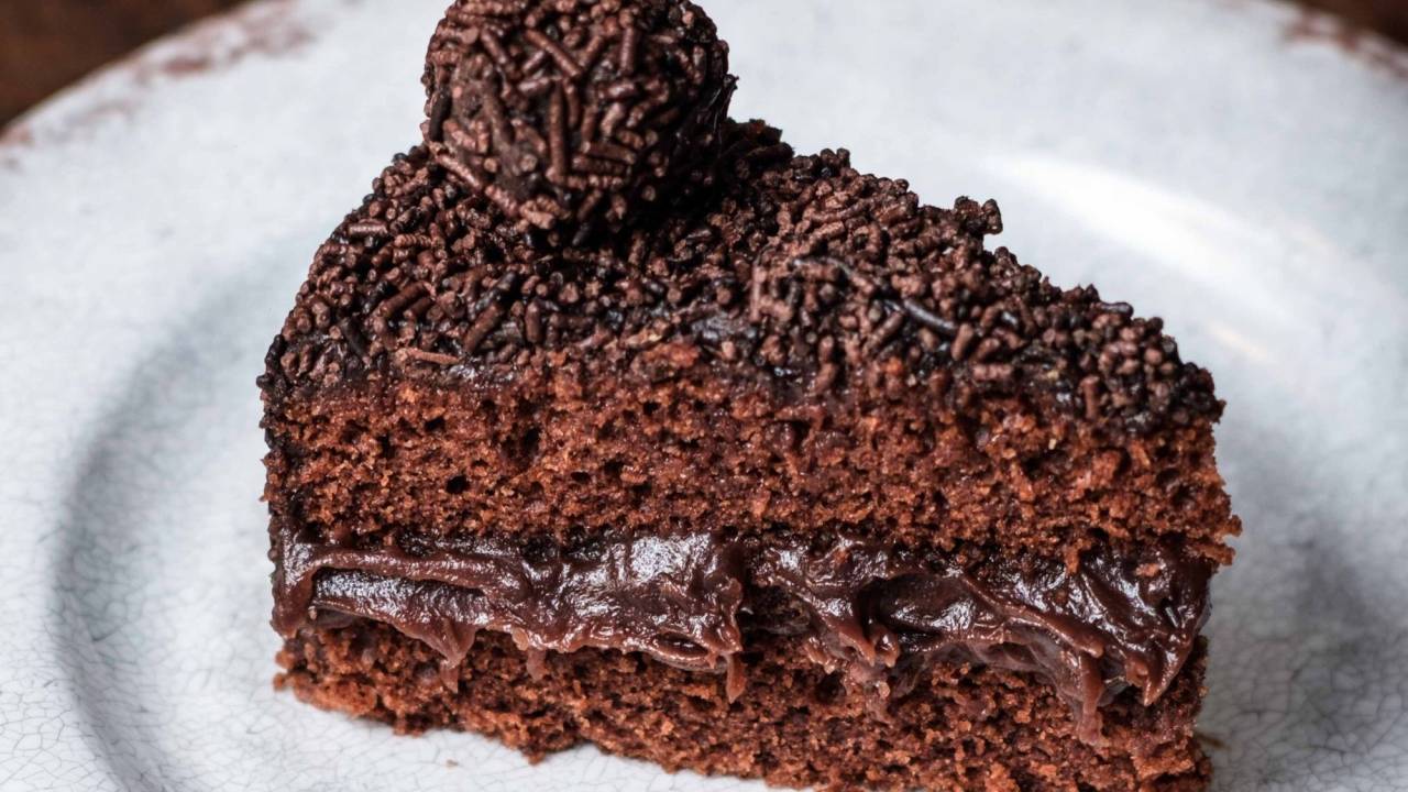 imagem mostra bolo de chocolate recheado com brigadeiro e cobertura de chocolate com granulada e um brigadeiro enrolado em cima