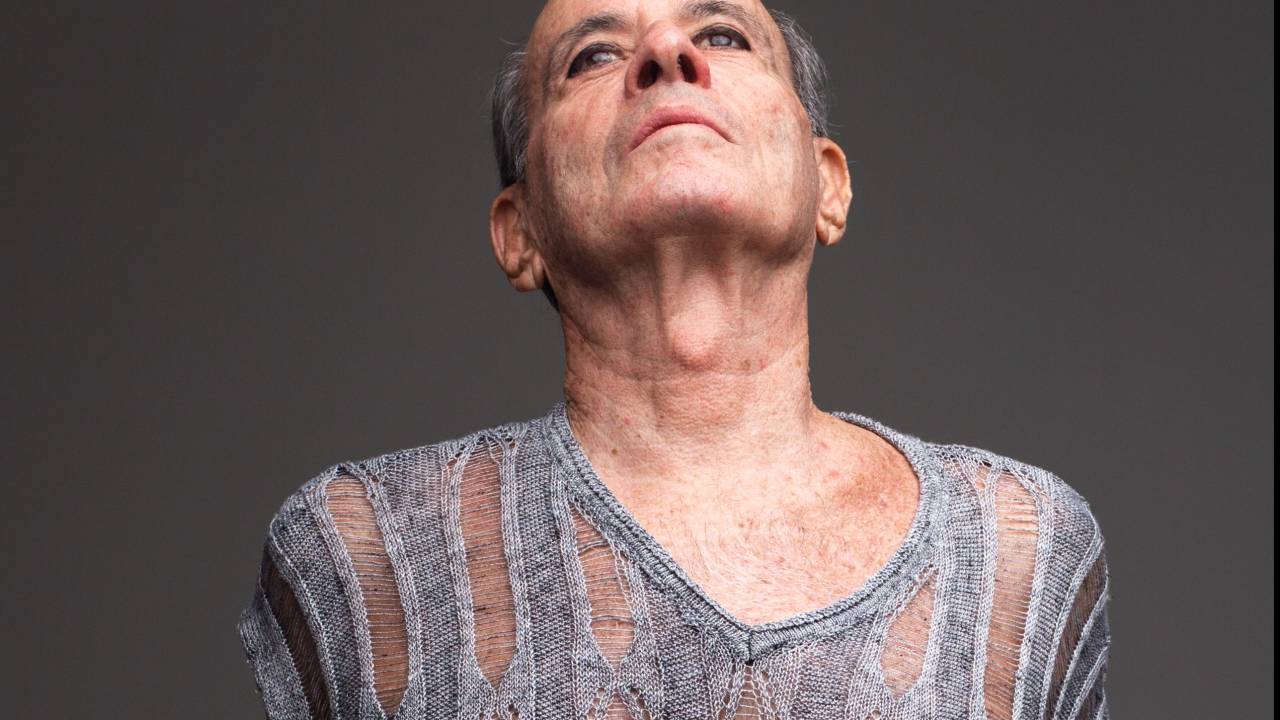 Ney Matogrosso usa blusa cinza listrada com tecido transparente