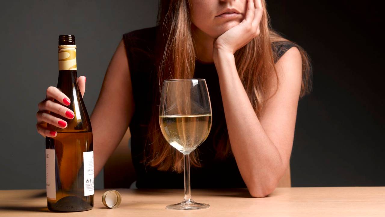 Mulher diante de uma garrafa de vinho e uma taça cheia.