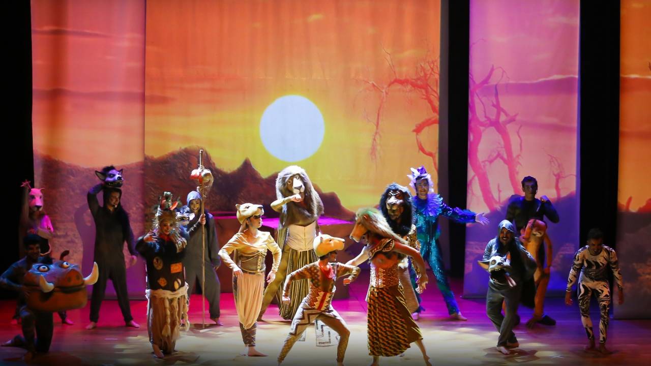 Foto mostra atores fantasiados no palco do espetáculo O Rei Leão