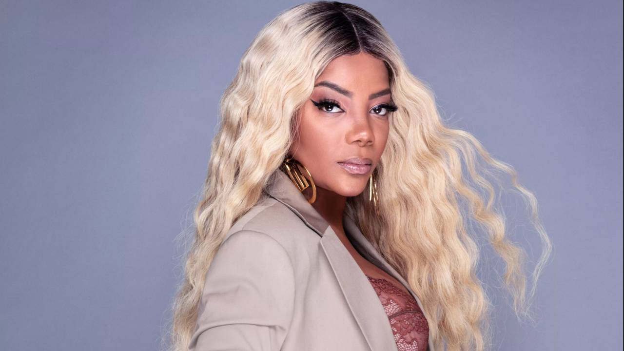 Ludmilla de peruca loura e paletó cinza