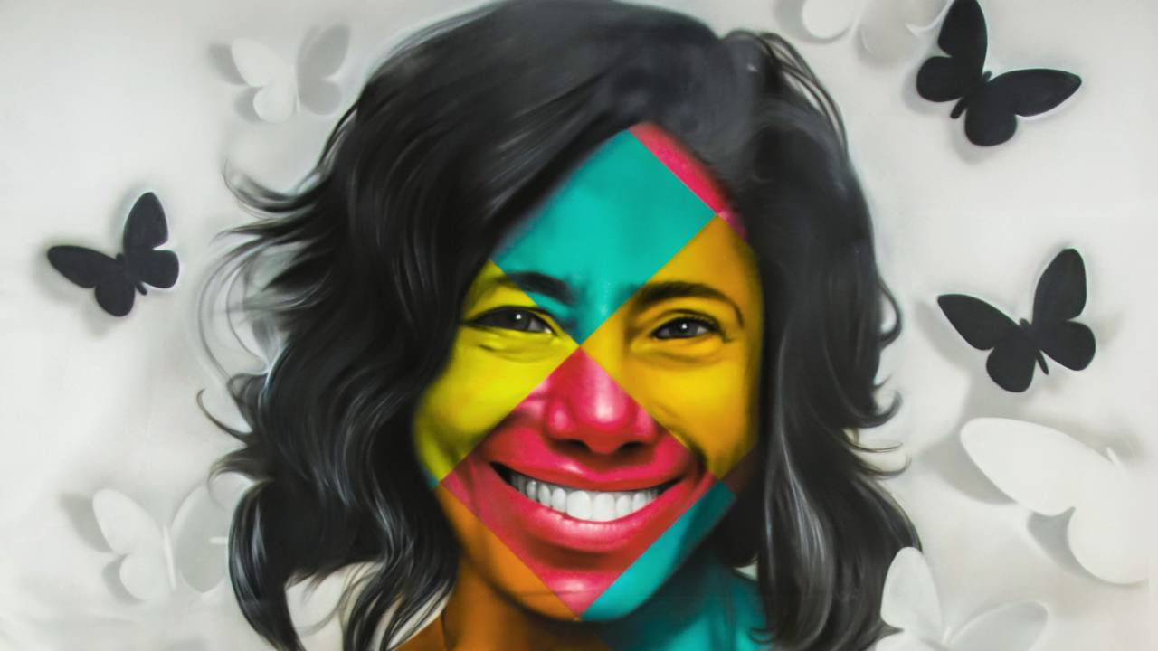 Glória Maria aparece toda colorida, usando camisa branca, cercada de borboletas pretas e segurando o planeta Terra