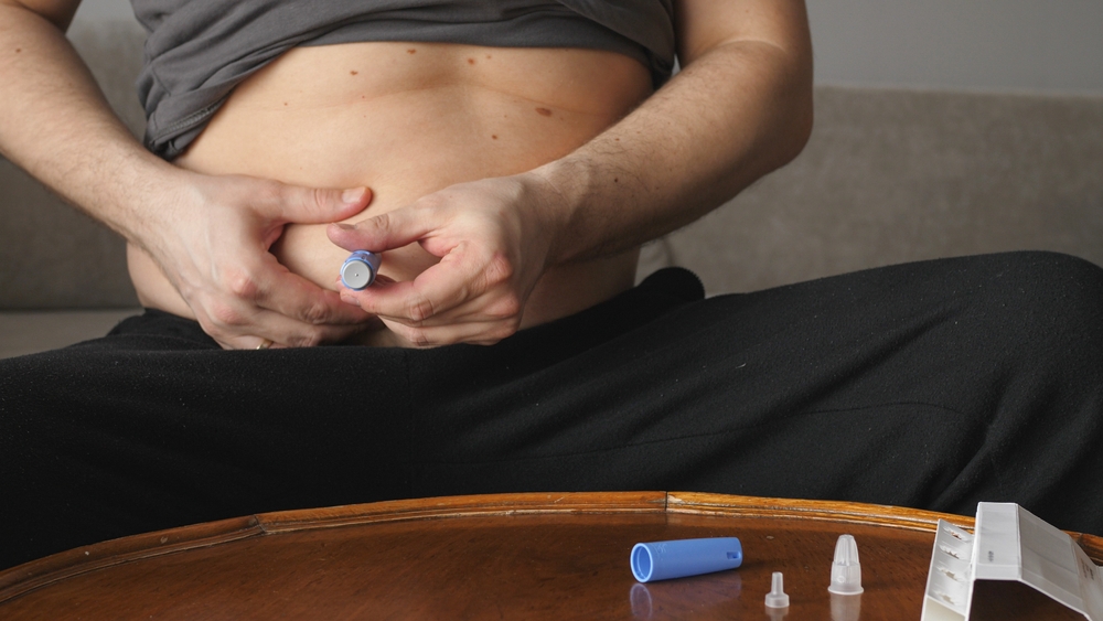 Homem sentado aplica remédio na barriga.