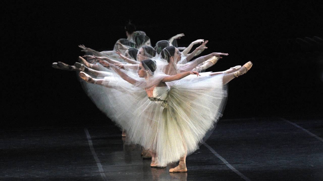 Imagem traz bailarinas de lad, levantando uma das pernas e um dos braços, uma para a esquerda seguida da outra, atrás, para a direita. Elas usam roupa branca, com tutu.