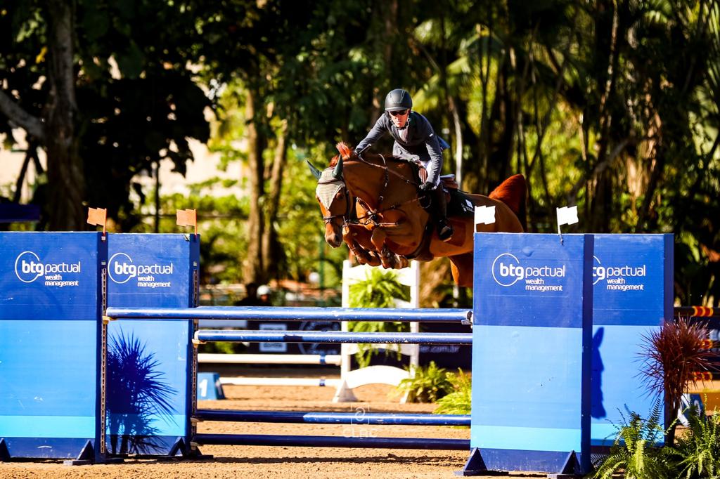 Cavaleiro está sob seu cavalo e diante de obstáculo azul