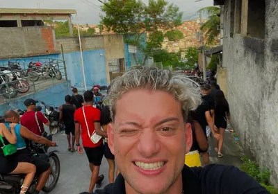 Foto mostra youtuber com cabelo pintado de loiro fazendo selfie em favela carioca