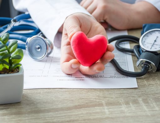 Um homem uniformizado de médico segura um coração de borracha em um ambiente clínico.