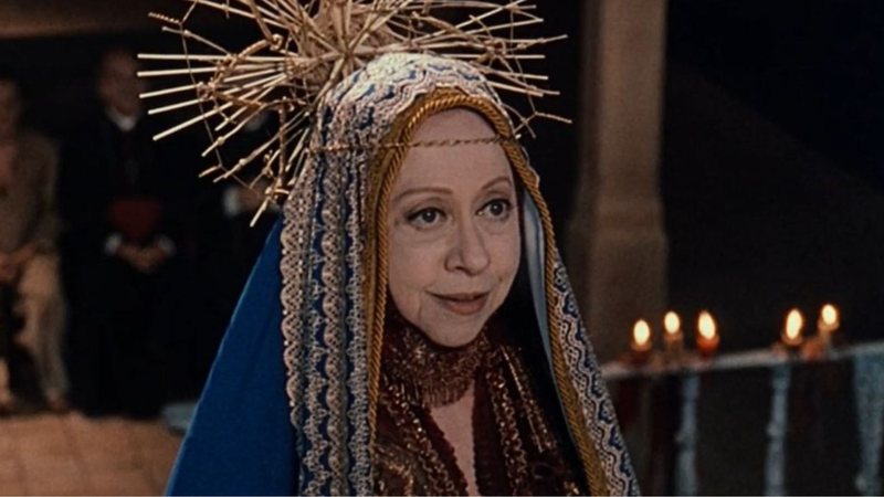 Fernanda Montenegro é uma mulher branca. Ela usa um manto azul com bordado dourado e coroa dourada