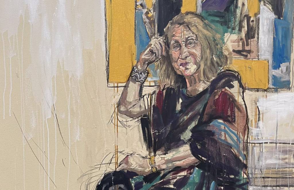 23071901 Anna Bella Geiger, série Artistas no Ateliê-9 Panmela Castro Pintura traz Anna Bella Geiger, uma mulher branca, idosa, de cabelos compridos, usando vestido preto, sentada em uma cadeira e com quadro ao fundo