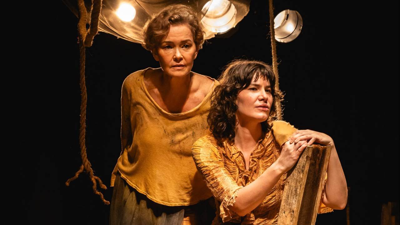 à esquerda, Julia Lemmertz, mulher branca, com cabelo curto alourado. Ela usa blusa dourada. À direita, Luiza Lemmertz, com cabelo médio e castanho. Também de roupa dourada.