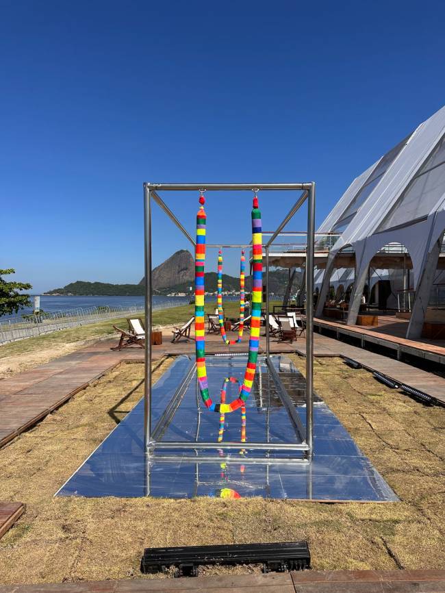Toz – escultura ArtRio3 Balanço em aço com cordas revestidas de tecidos coloridos. Ao fundo, de longe, o céu azul e o Morro da Urca.