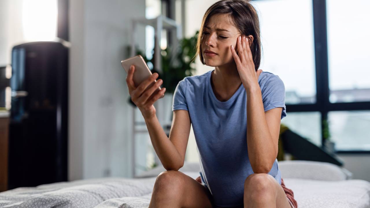 Mulher preocupada olha para o telefone celular.