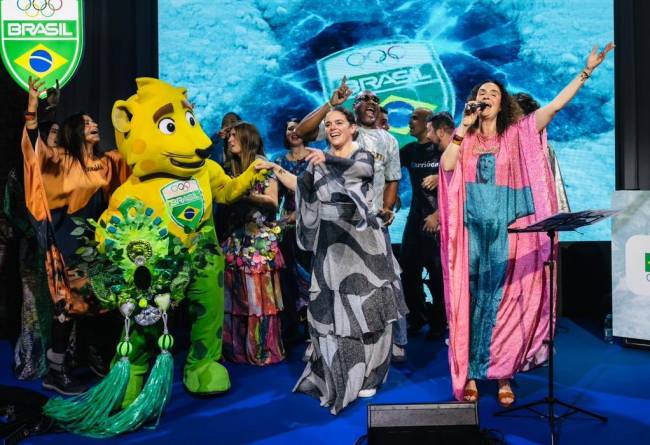 O mascote Ginga segura as m&atilde;os de Manoela Penna, do COB, a estilista Alessa e a equipe do Time Brasil