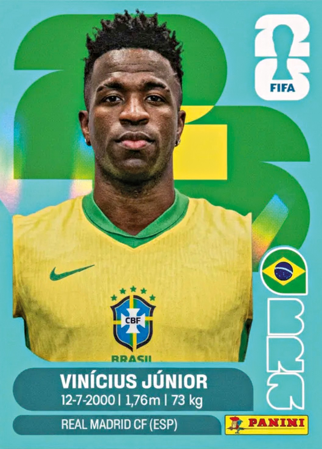Vin&iacute;cius J&uacute;nior, jogador de futebol negro, com cabelo crespo e barba rala, vestindo camisa amarela da sele&ccedil;&atilde;o brasileira com gola verde, olhando para frente. Ao fundo, elementos gr&aacute;ficos verdes e amarelos sobre azul claro, com o logo da FIFA e da Panini, al&eacute;m de informa&ccedil;&otilde;es sobre o atleta: data de nascimento, altura, peso e clube