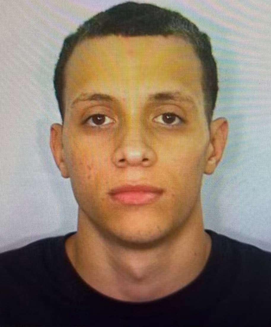 Rosto de um homem jovem, pele clara, cabelo curto e escuro, olhos castanhos, boca fechada, vestindo camiseta preta, olhando diretamente para frente com express&atilde;o s&eacute;ria