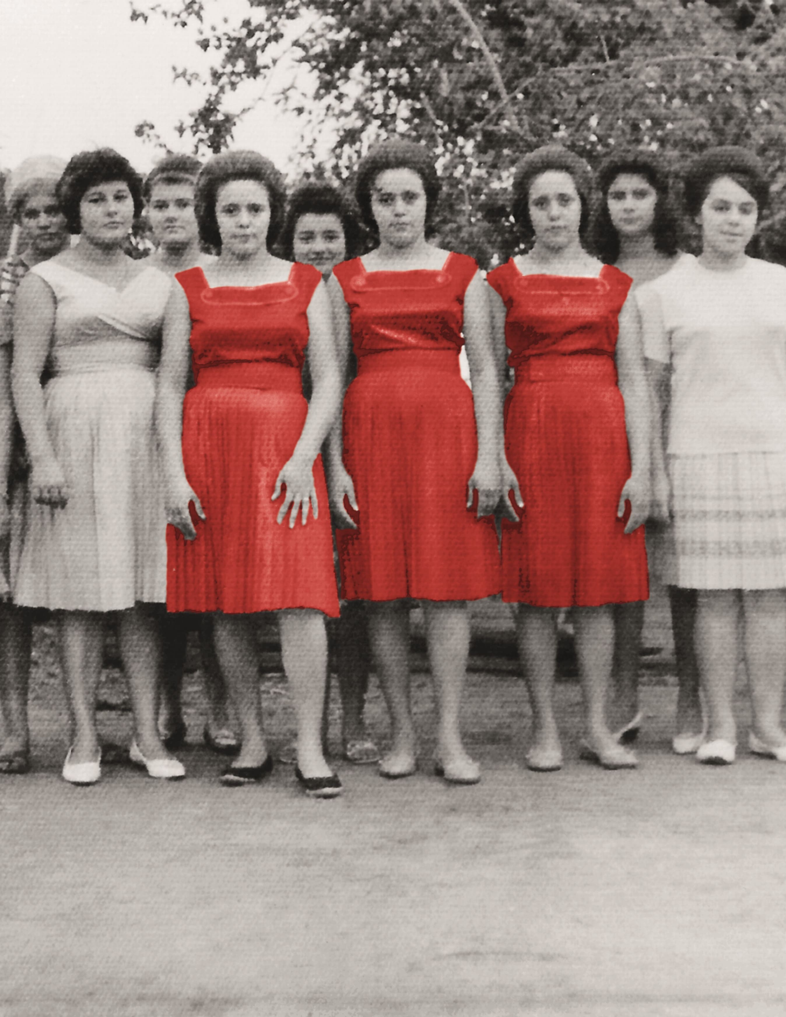 Grupo de dez mulheres jovens, algumas sorrindo, posando em fila. Tr&ecirc;s delas, no centro, usam vestidos vermelhos vibrantes, contrastando com as outras em tons de cinza e branco. O fundo &eacute; uma folhagem escura