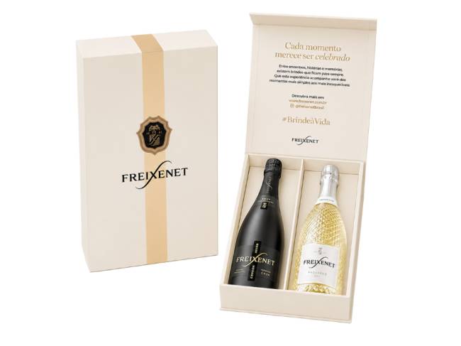 Caixa de presente Freixenet bege com faixa dourada e bras&atilde;o, contendo duas garrafas de espumante: uma preta Cordon Negro e uma branca Prosecco. A tampa aberta exibe a mensagem Cada momento merece ser celebrado e a hashtag #Brinde&agrave;Vida
