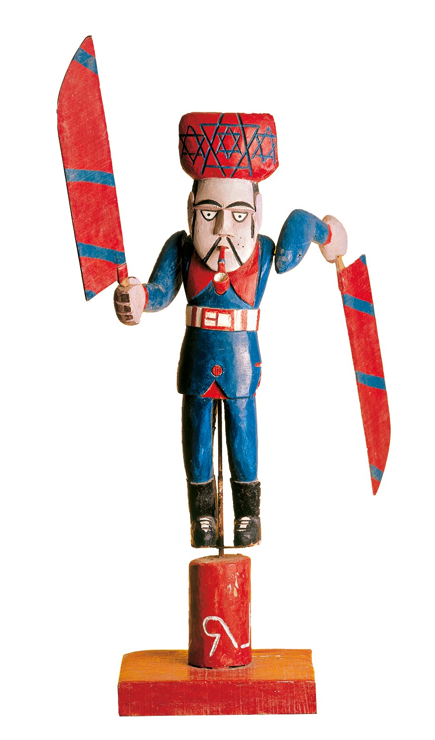 Boneco de madeira colorido, representando um homem com chap&eacute;u vermelho decorado com estrelas de seis pontas, bigode e cachimbo. Ele veste um uniforme azul com detalhes vermelhos e brancos, segurando uma faca vermelha com listras azuis em cada m&atilde;o. A figura est&aacute; sobre uma base de madeira vermelha e marrom, com um s&iacute;mbolo branco na parte inferior
