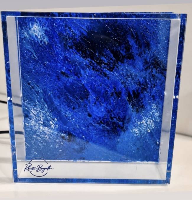 Objeto de arte em acr&iacute;lico transparente, formato cubo, com interior preenchido por uma textura abstrata em tons de azul escuro e branco, simulando ondas ou &aacute;gua em movimento. Na base frontal, uma assinatura em caligrafia preta: R. Bygth