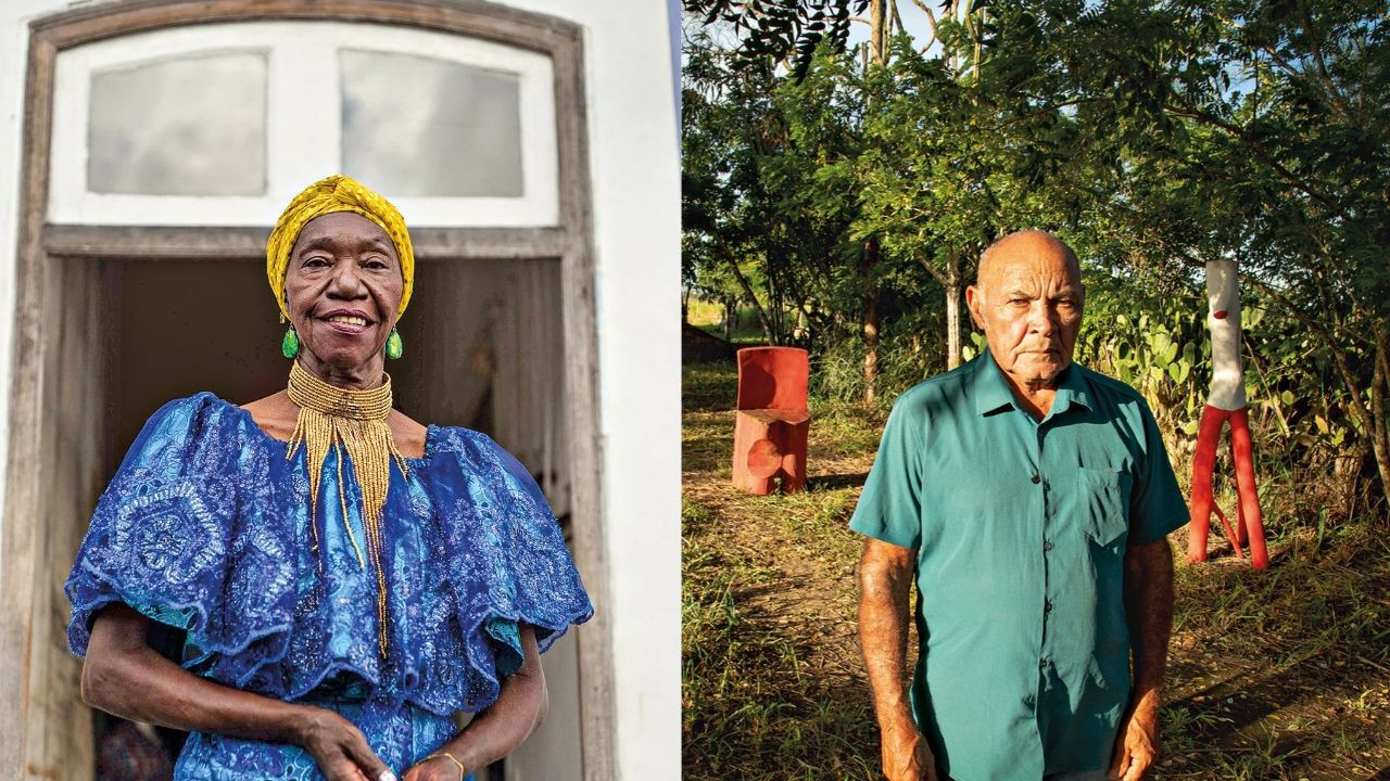 Mulher negra sorrindo, com turbante amarelo, brincos verdes e colar dourado, em frente a uma janela branca. Ao lado, homem pardo s&eacute;rio, de camisa verde, em um jardim com &aacute;rvores e esculturas vermelhas