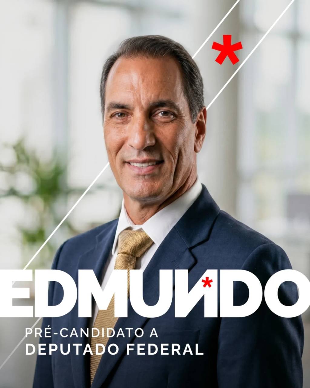 Homem de pele morena, cabelo escuro penteado para tr&aacute;s, sorrindo, vestindo terno azul-marinho e gravata dourada. O nome EDMUNDO em letras brancas grandes e PR&Eacute;-CANDIDATO A DEPUTADO FEDERAL em letras menores brancas aparecem sobre a imagem. Um asterisco vermelho est&aacute; no canto superior direito e outro sobre a letra U de EDMUNDO